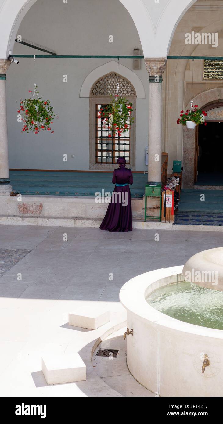 Donna in abiti tradizionali sotto i fiori nel cortile della Moschea degli imperatori nella città di Sarajevo, Bosnia ed Erzegovina, 10 settembre 2023 Foto Stock