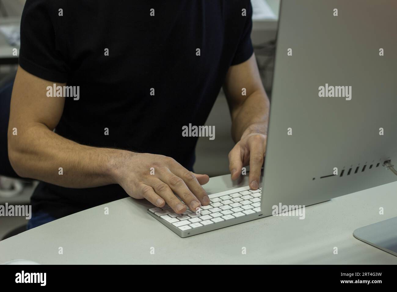 Giovane uomo con una maglietta nera che lavora con il computer, le mani dell'uomo sul computer della tastiera Foto Stock