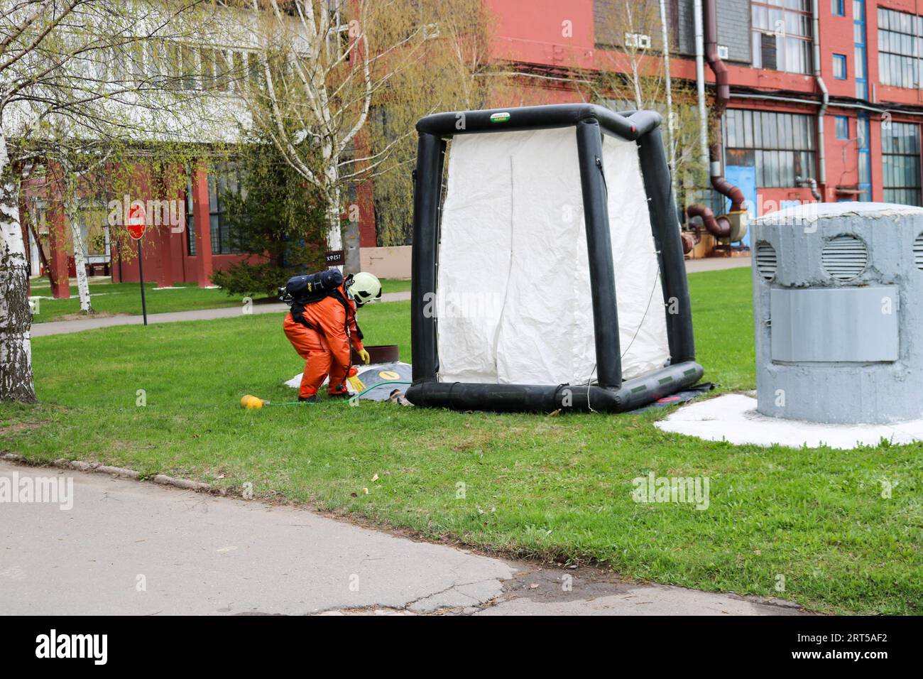 Un pompiere professionale in una speciale tuta ignifuga arancione si prepara ad assemblare una tenda ad ossigeno bianco per salvare le persone in una raffineria chimica, petrolifera, Foto Stock