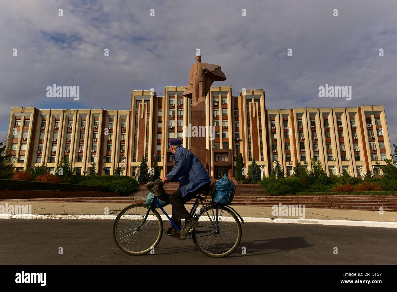 Vestita in modo appropriato, in bicicletta di fronte all'edificio del governo della Transnistria a Tiraspol, la capitale dello stato de facto Foto Stock