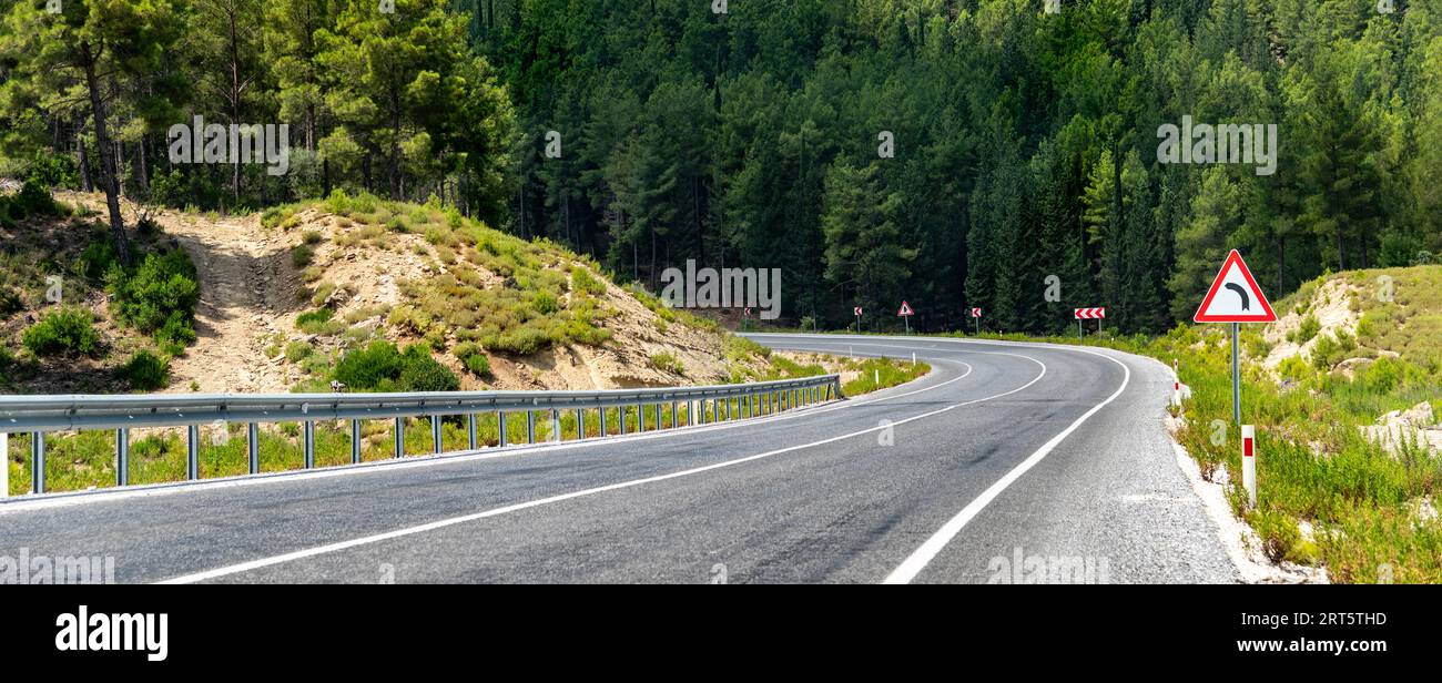 Strada asfaltata curva che passa attraverso la foresta in una giornata di sole Foto Stock