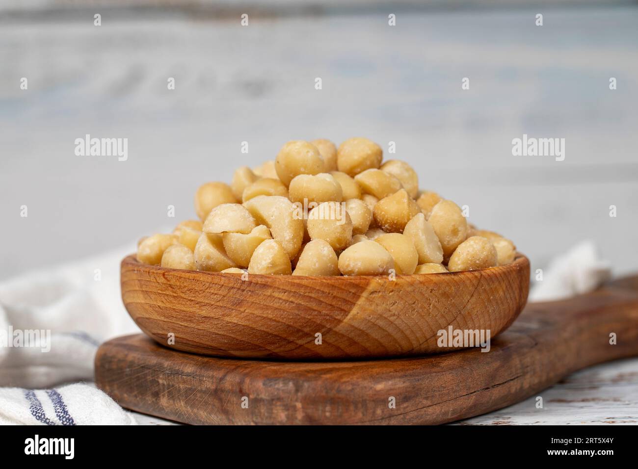 Noce di macadamia in un recipiente di legno. Noci di macadamia sbucciate su fondo di legno bianco Foto Stock