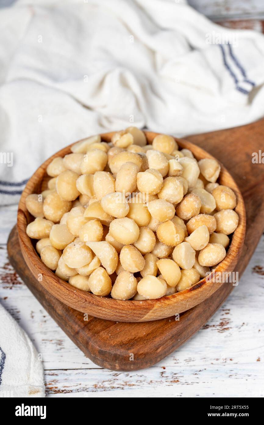 Noce di macadamia in un recipiente di legno. Noci di macadamia sbucciate su fondo di legno bianco Foto Stock
