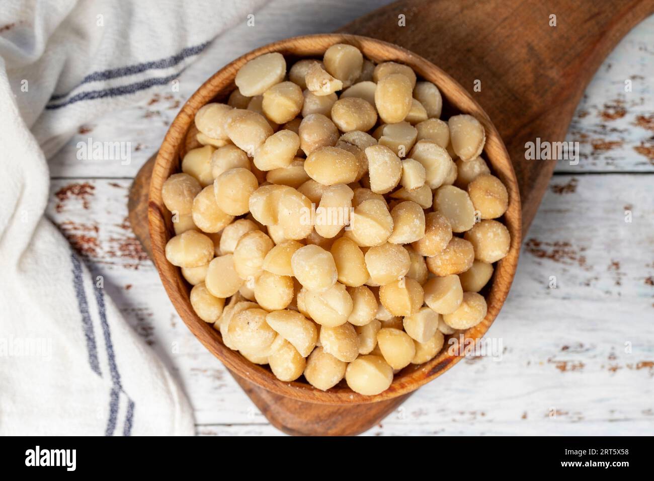 Noce di macadamia in un recipiente di legno. Noci di macadamia sbucciate su fondo di legno bianco. Vista dall'alto Foto Stock