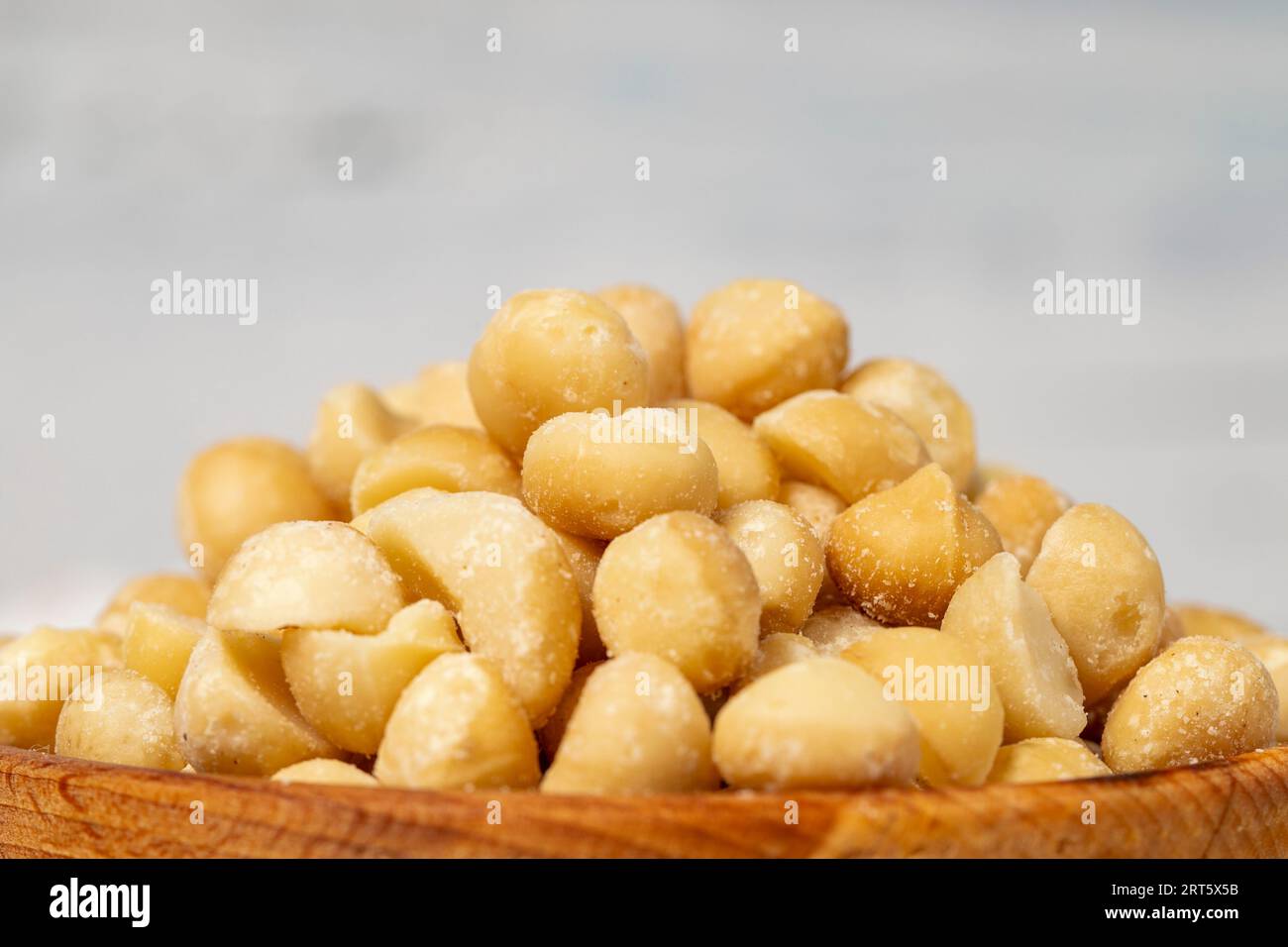 Noce di macadamia in un recipiente di legno. Noci di macadamia sbucciate su fondo di legno bianco. Primo piano Foto Stock