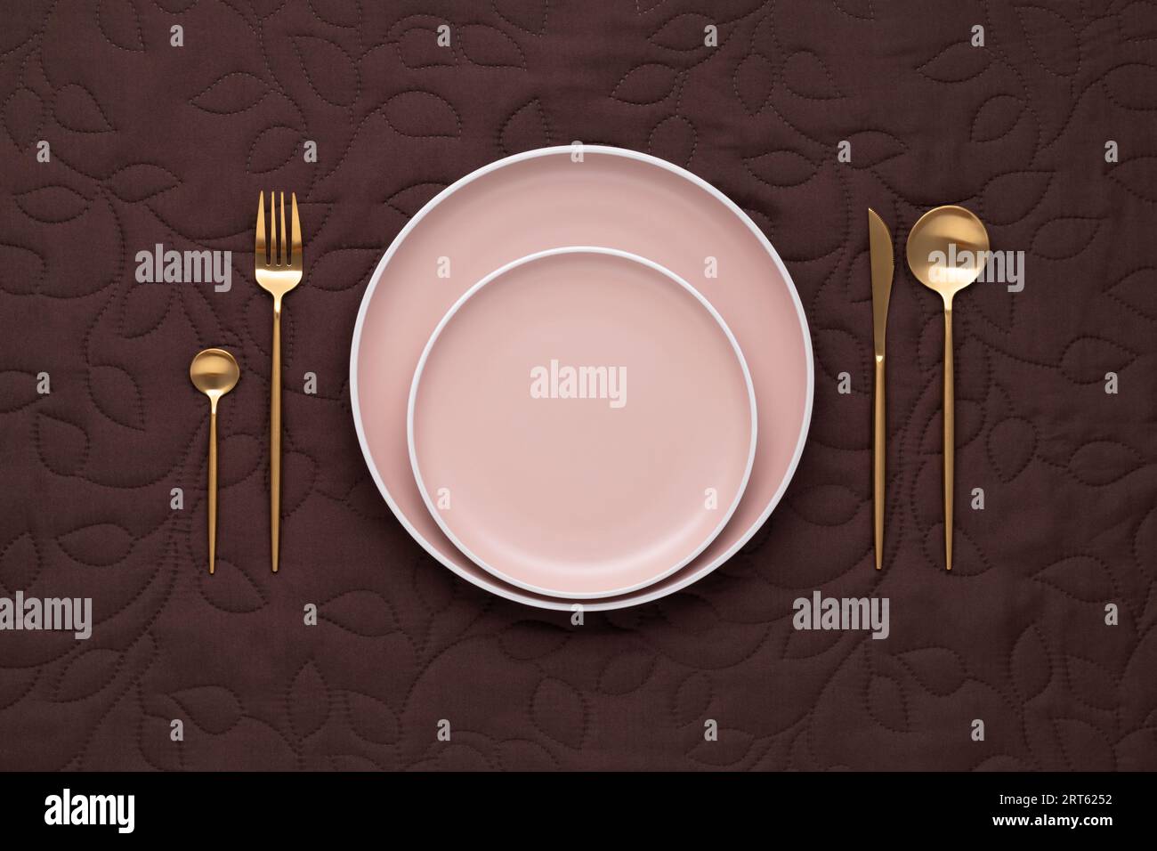 Tavolo festivo. Forchetta dorata, coltello e cucchiaio. Piastra in ceramica vuota con posate in oro. Tovaglia marrone scuro. Vista dall'alto. Cena nel lussuoso ristorante restaura Foto Stock