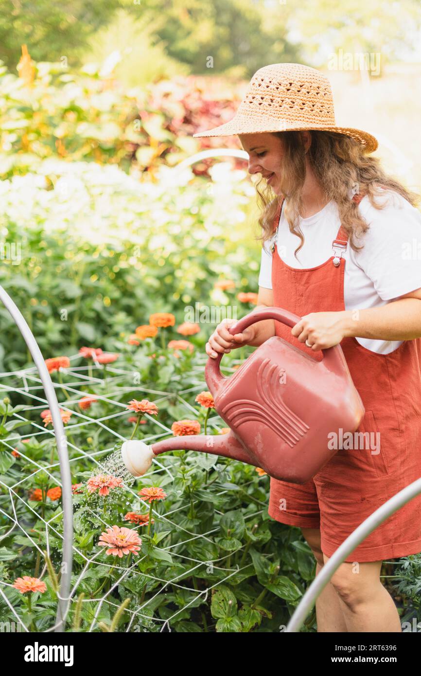 Una donna che annaffiava fiori rossi nel suo giardino con un'annaffiatura rossa Foto Stock