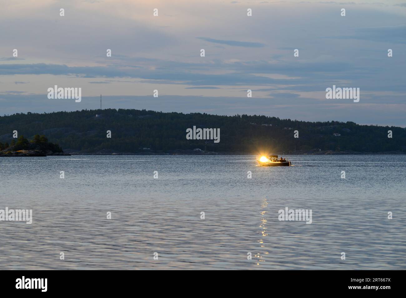 Il sole serale si riflette sul parabrezza di una tradizionale barca da diporto che naviga attraverso il mare con l'isola Fluer sullo sfondo, Telemark, Norvegia. Foto Stock