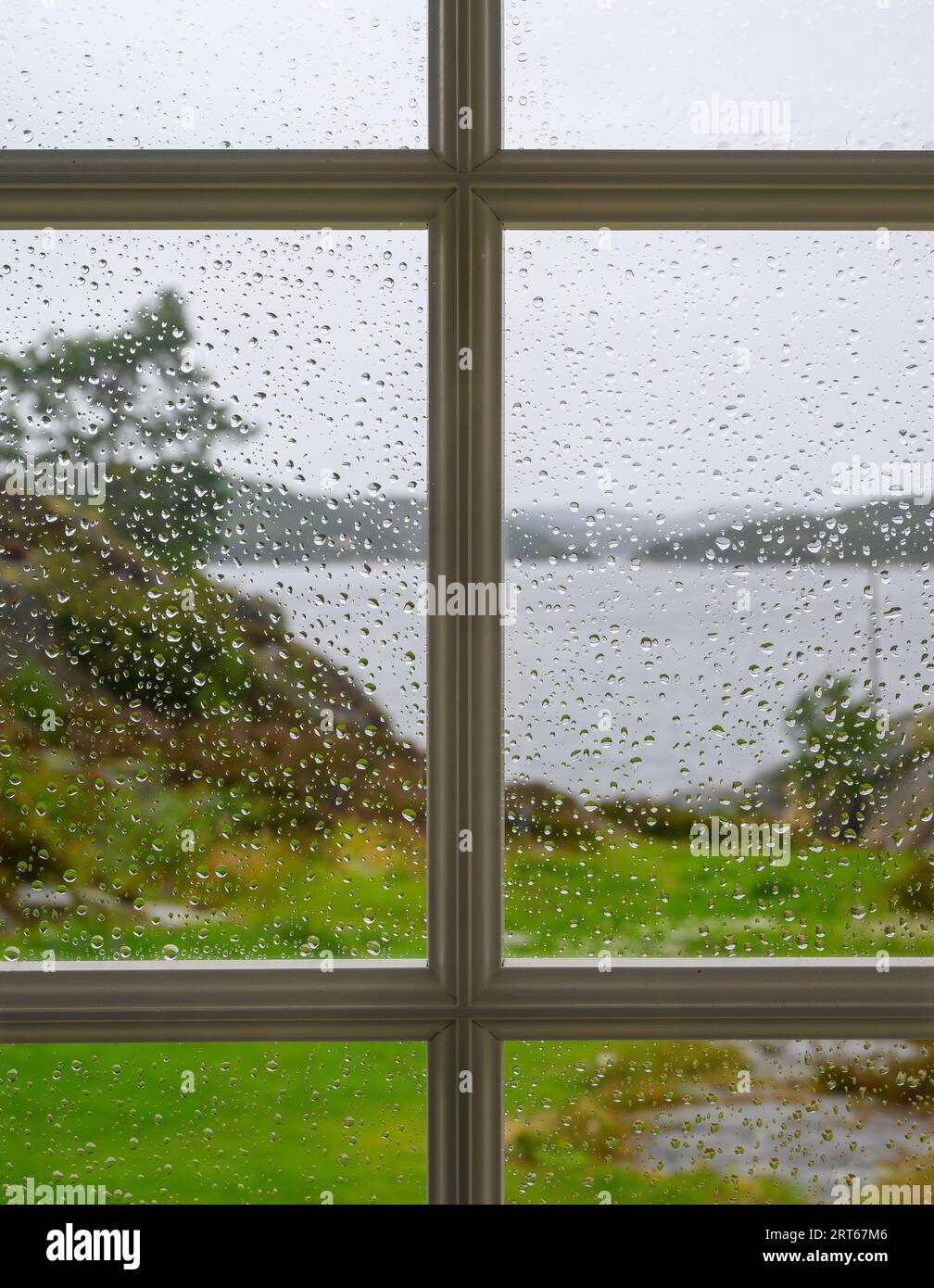 Vista dall'interno verso l'esterno: Vista del paesaggio sfocato (sfocato), del mare e delle isole attraverso una finestra piena di gocce di pioggia a fuoco. Telemark, Norvegia. Foto Stock