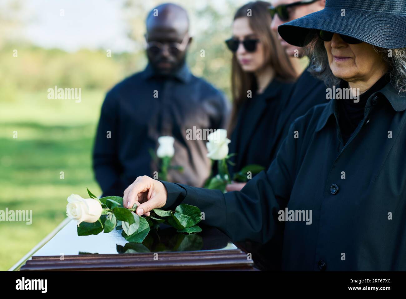 Donna matura addolorata in abiti in lutto che mette una rosa bianca sulla bara mentre esprime simpatia per la morte della persona cara Foto Stock