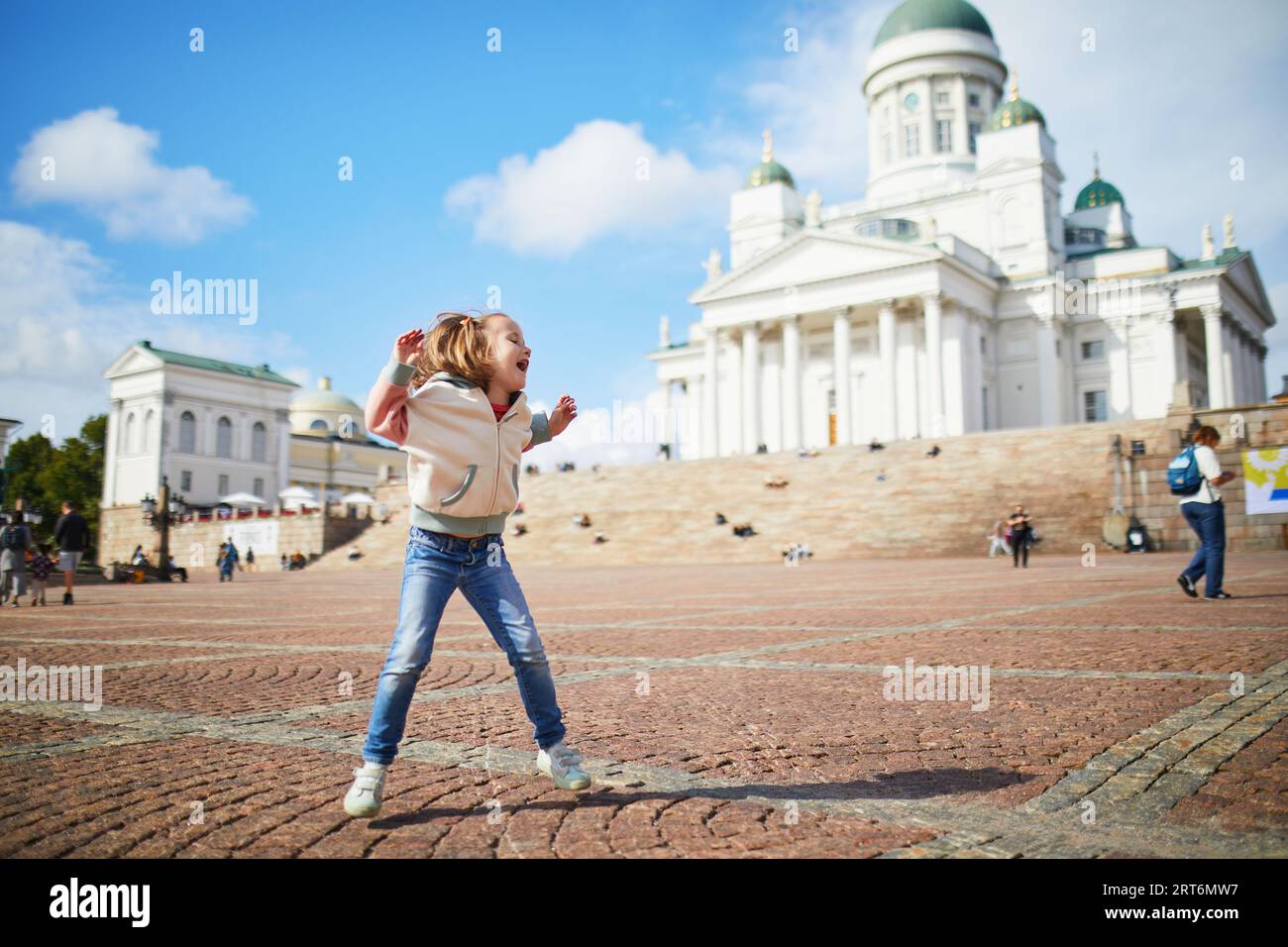 Adorabile ragazza prescolare che salta vicino alla cattedrale di Helsinki (Helsingin tuomiokirkko) su Senaatintori a Helsinki, Finlandia. Viaggiare con il concetto dei bambini Foto Stock
