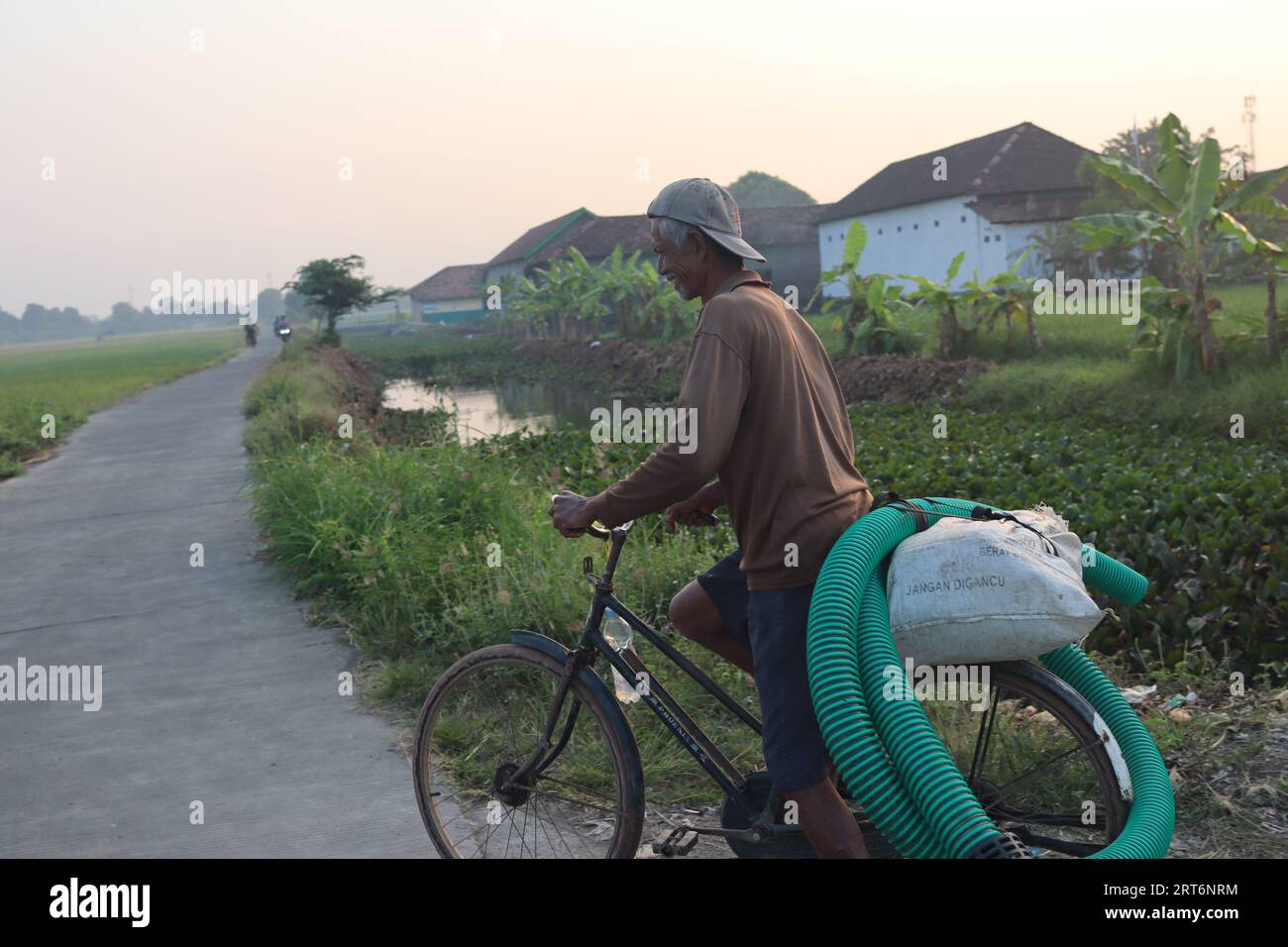 Persone in bicicletta verso i campi di riso con tubi dell'acqua Foto Stock