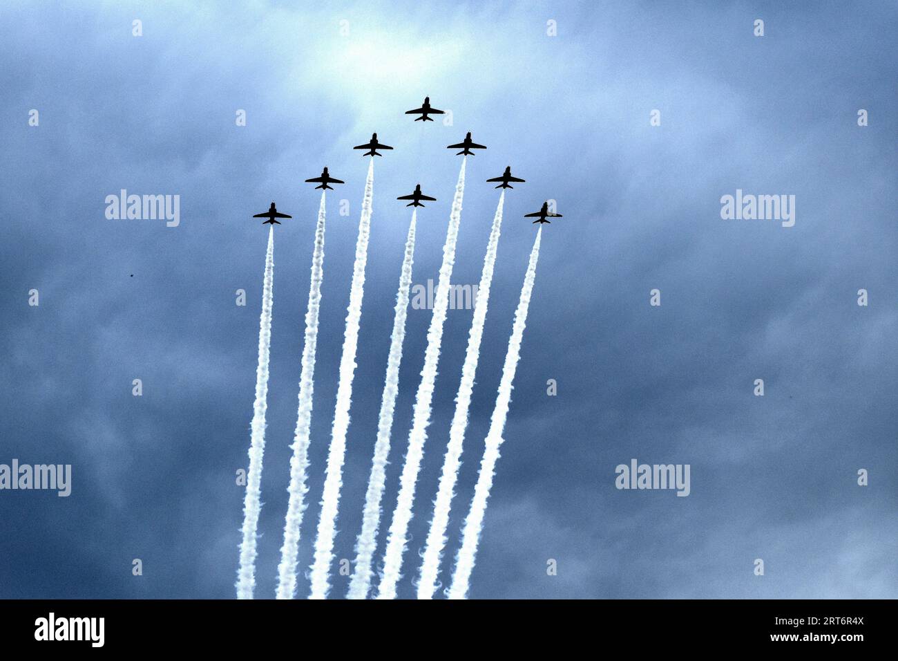 Un'immagine di diversi aerei in formazione che volano attraverso il cielo, con sentieri di fumo bianchi e ondeggianti che seguono ciascuno di essi Foto Stock