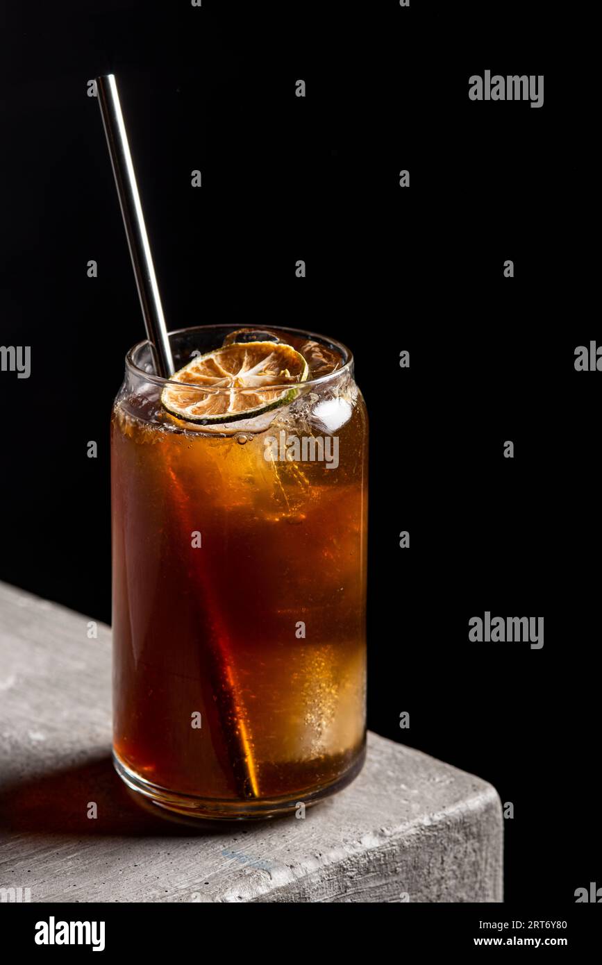Cocktail alcolico rinfrescante in bicchiere con cubetti di ghiaccio e paglia guarnita con fetta di lime secca posta su un tavolo di pietra Foto Stock