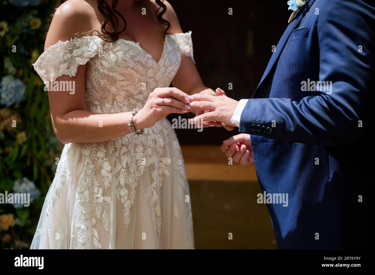 Anonimo coppia in abiti da sposa eleganti che si tengono le mani delicatamente mentre si alzano e si scambiano anelli durante la celebrazione del matrimonio Foto Stock