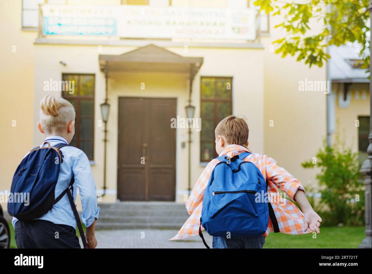 i bambini che corrono a scuola con gli zaini nelle giornate di sole. Inizio dell'anno accademico. Ragazzi vicino alla porta di scuola. Immagine con messa a fuoco selettiva Foto Stock