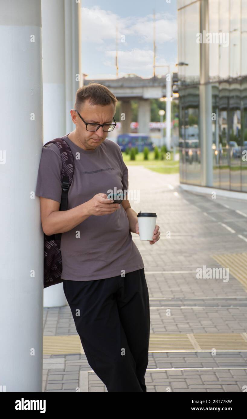un uomo con gli occhiali sembra tenace e insoddisfatto del suo cellulare per strada in città durante il giorno Foto Stock