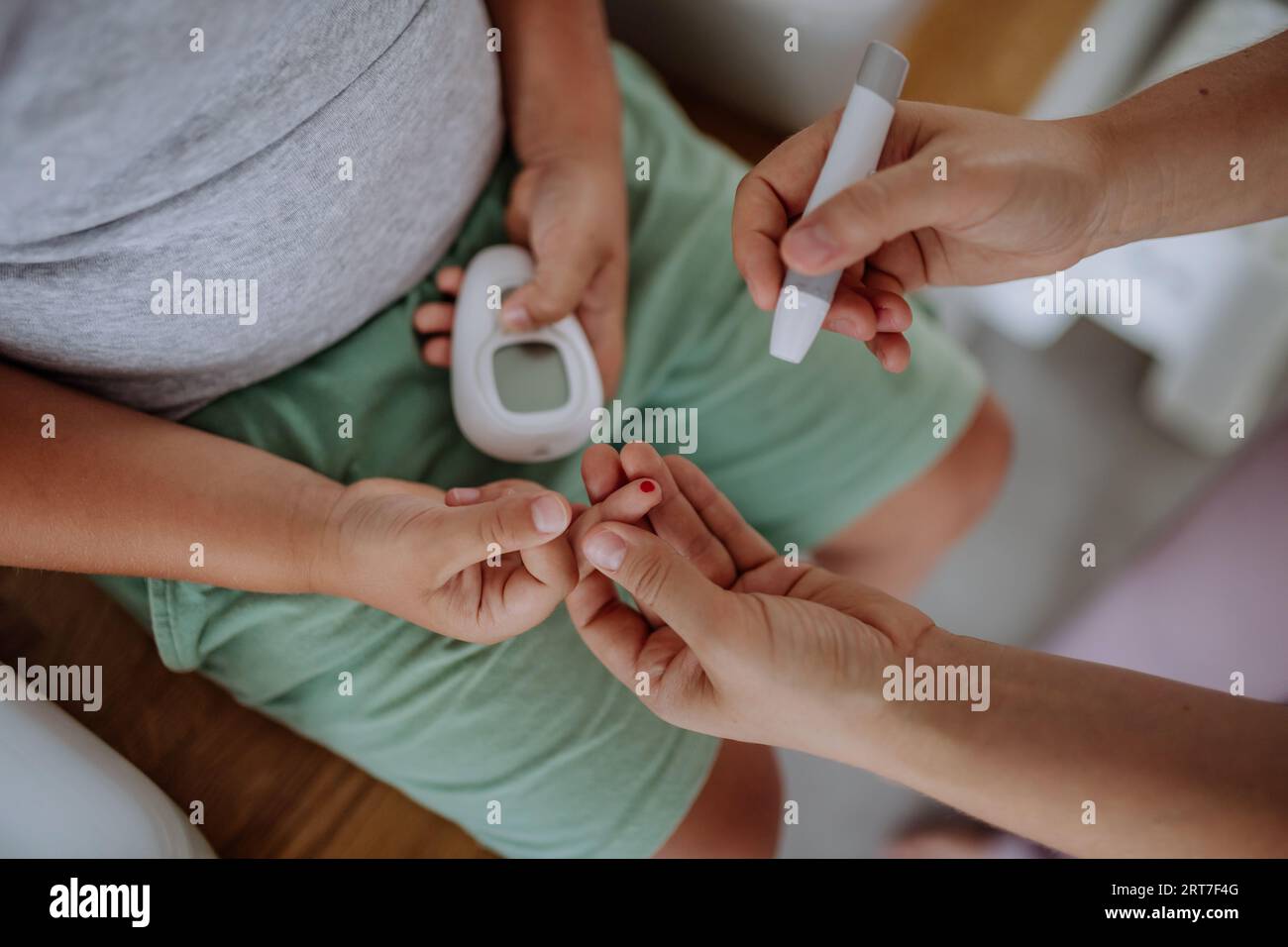 Madre che controlla il livello di glucosio nel sangue di suo figlio a casa usando un glucometro con il dito. Foto Stock