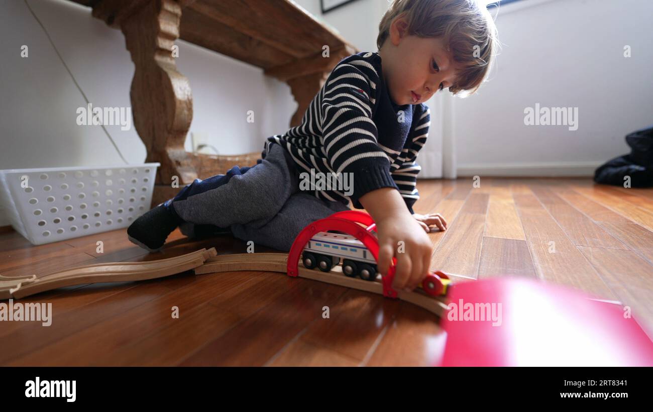 Il bambino gioca con i giocattoli del treno vintage retrò su binari di legno, un bambino caucasico che gioca da solo a casa Foto Stock