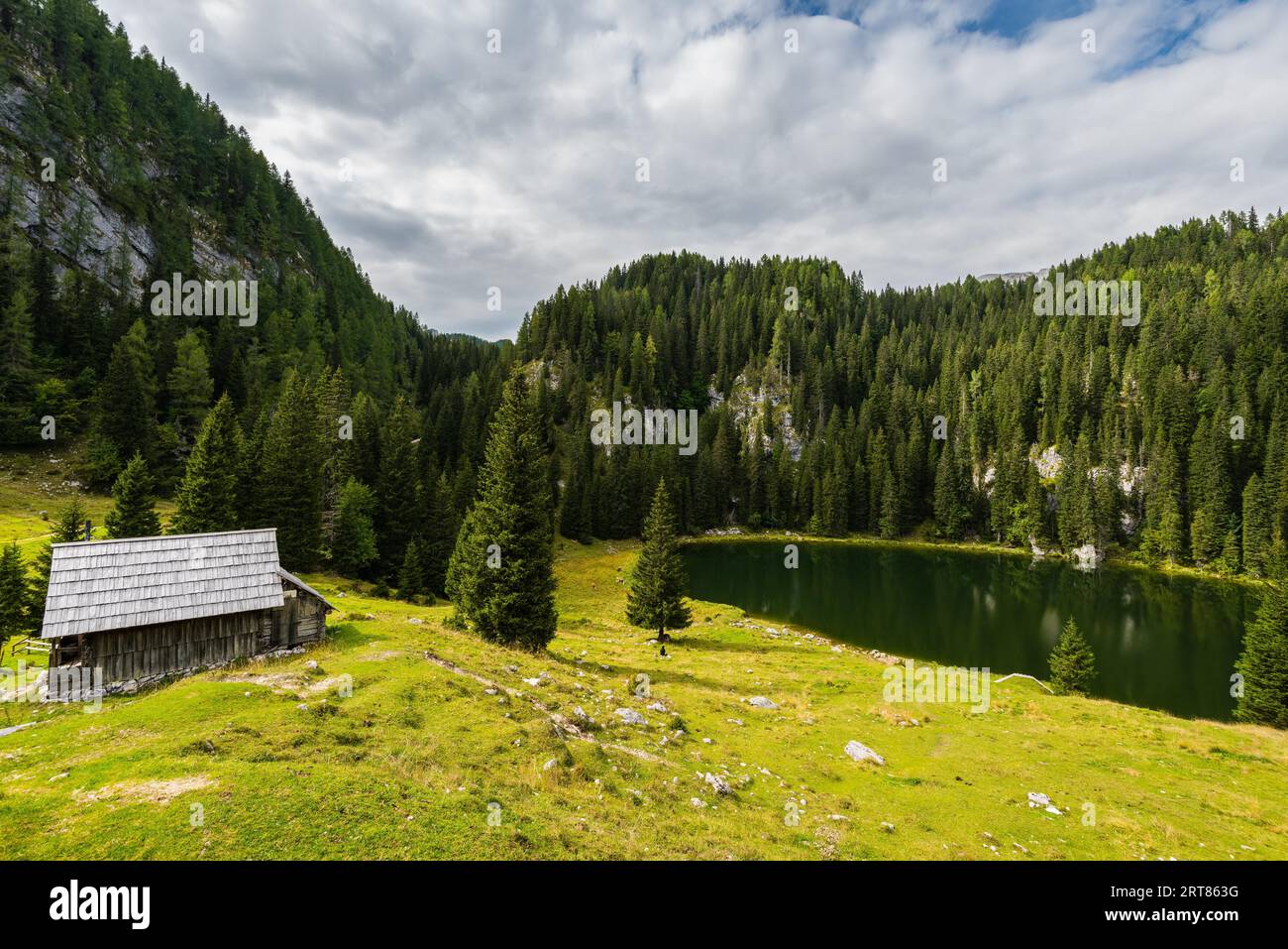 Capanne di tronchi e un lago di montagna nelle montagne di Le Alpi slovene sulla cima Planina Blato in piena di sole giorno con le nuvole Foto Stock