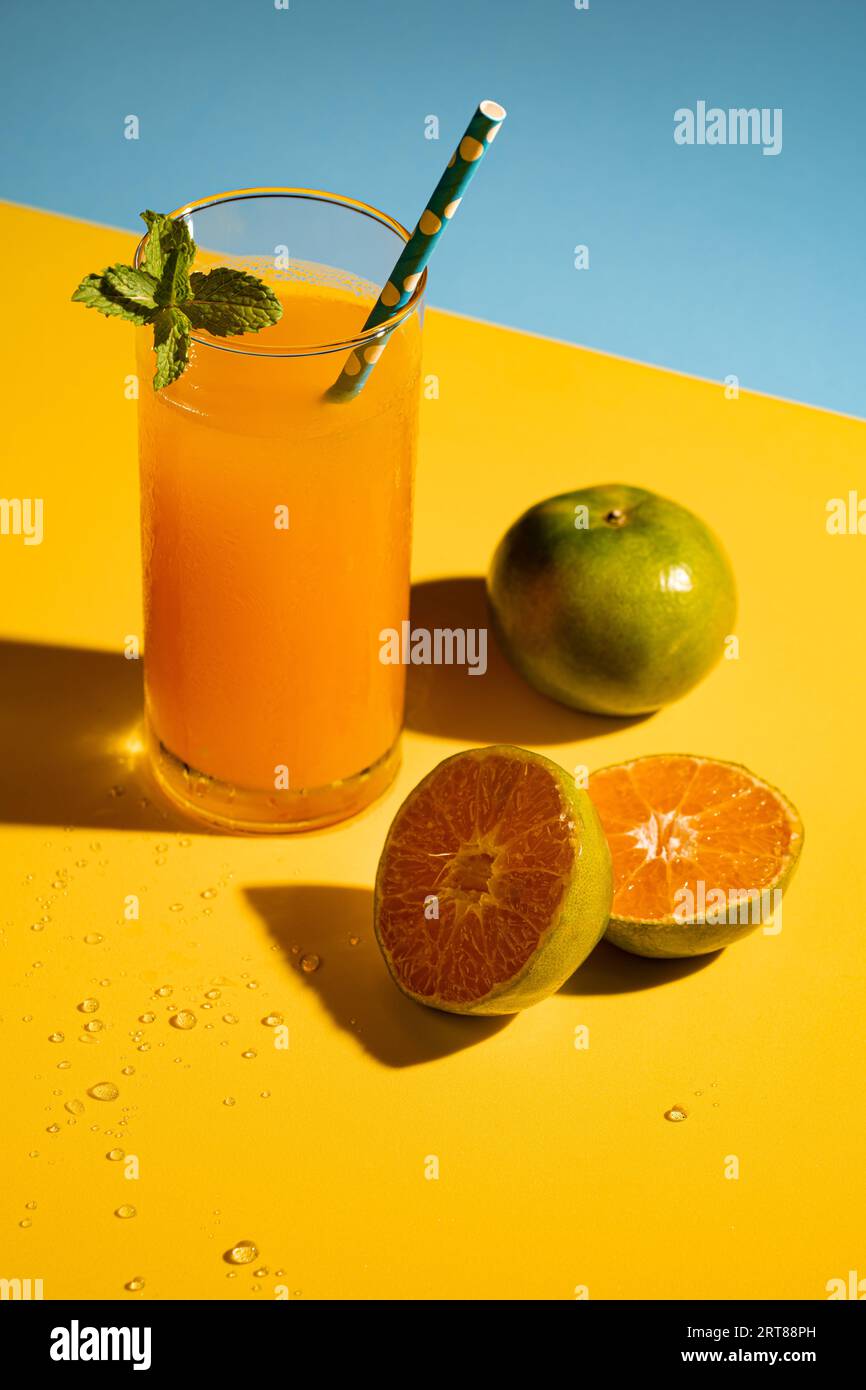 Succo di arance fredde appena spremute con ghiaccio su sfondo giallo-blu. Stile pop art. Foto Stock