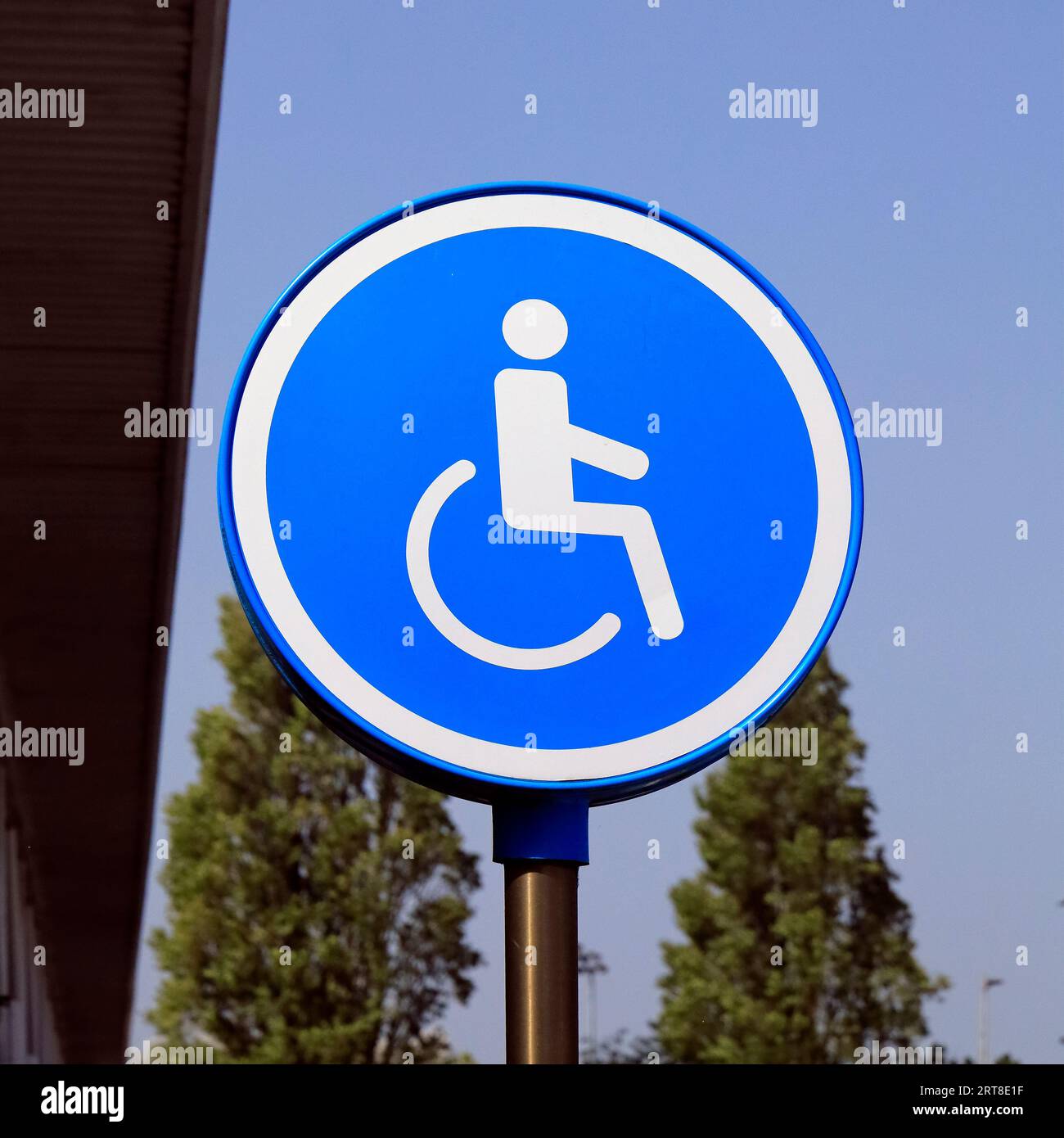 Parcheggio per disabili su un lato - uomo in sedia a rotelle su sfondo blu contro posti auto facilmente accessibili vicino agli ingressi Foto Stock