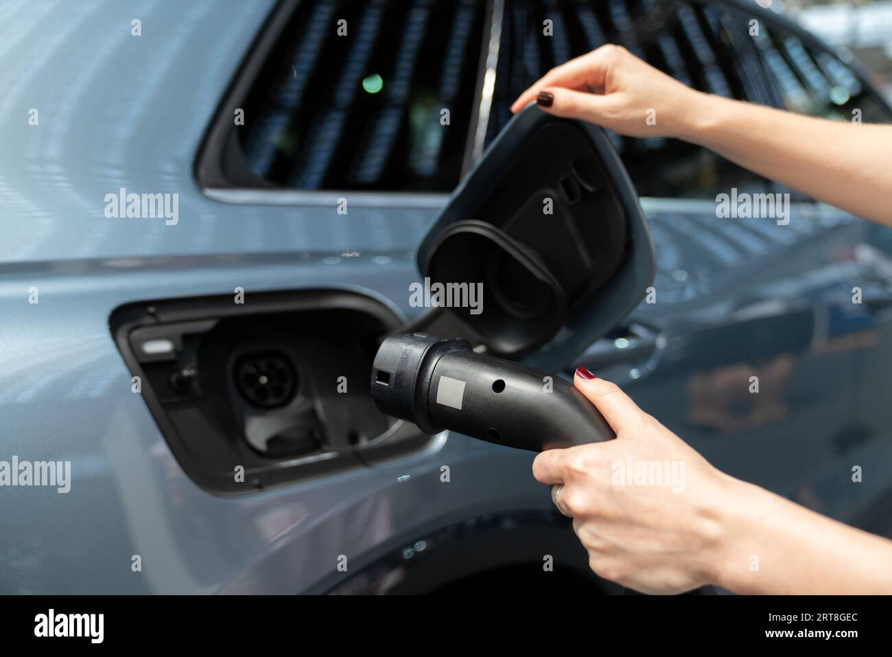 Donna che tiene la spina della stazione di ricarica per auto elettriche. Foto Stock