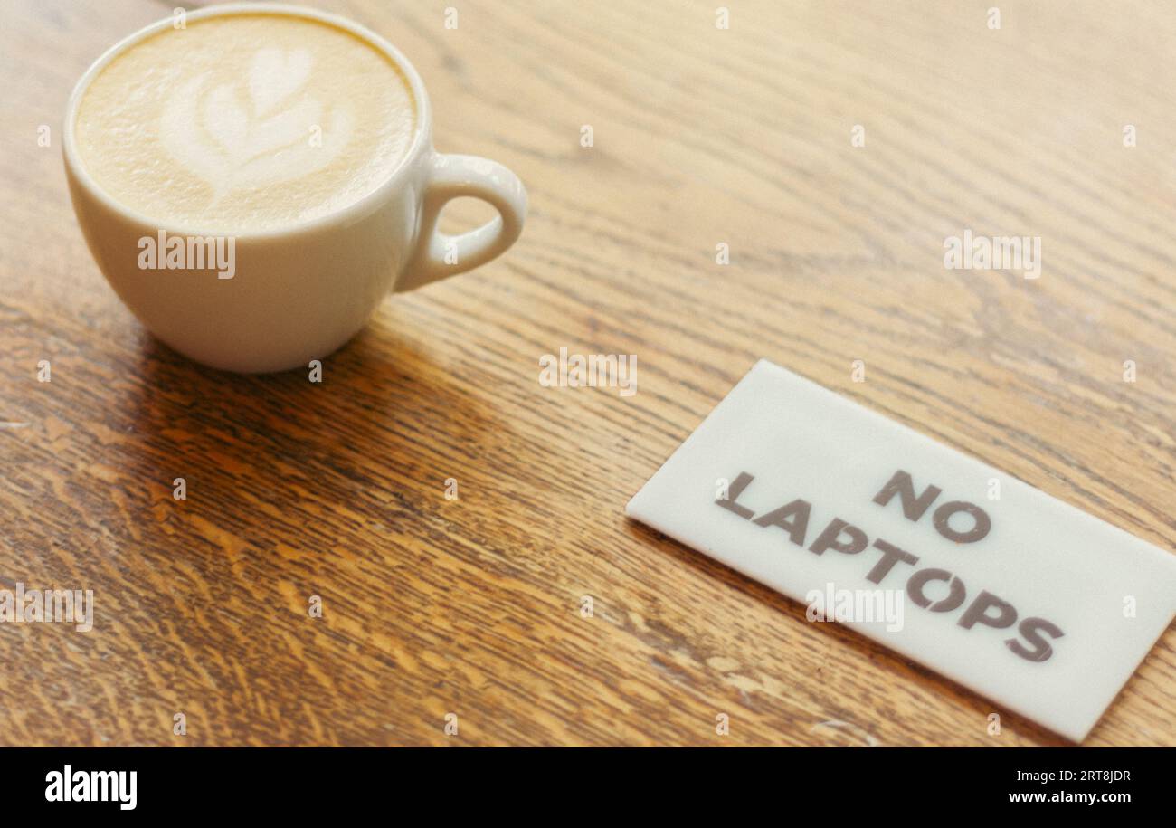 Tazza di caffè su un tavolo di legno e cartello "No Laptops". Caffè con latte in tazza bianca senza zona wi-fi. Tavolo per la colazione. Stile di vita moderno. Foto Stock