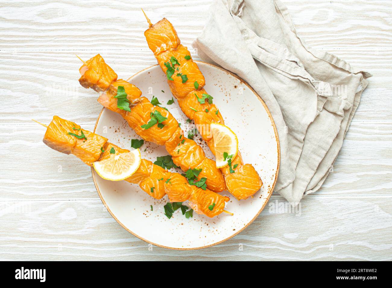 Spiedini di salmone alla griglia conditi con prezzemolo verde e limone su piatto di ceramica su tavola rustica in legno bianco vista dall'alto, salutare Foto Stock