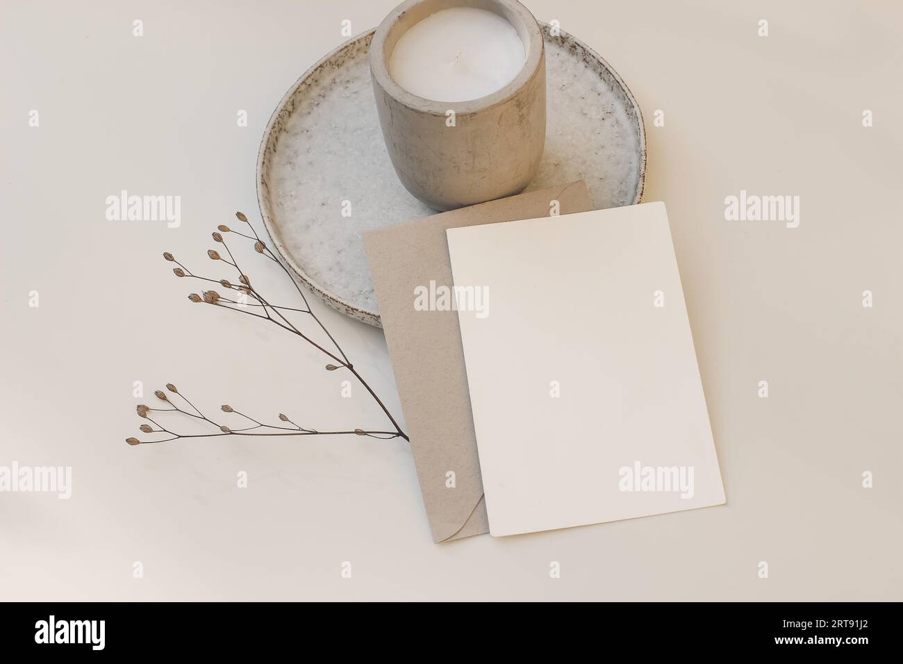 Cancelleria minimalista per Natale o autunno. Primo piano del biglietto d'auguri vuoto, modello di invito con busta. Candela in una tazza di cemento su piastra in ceramica Foto Stock