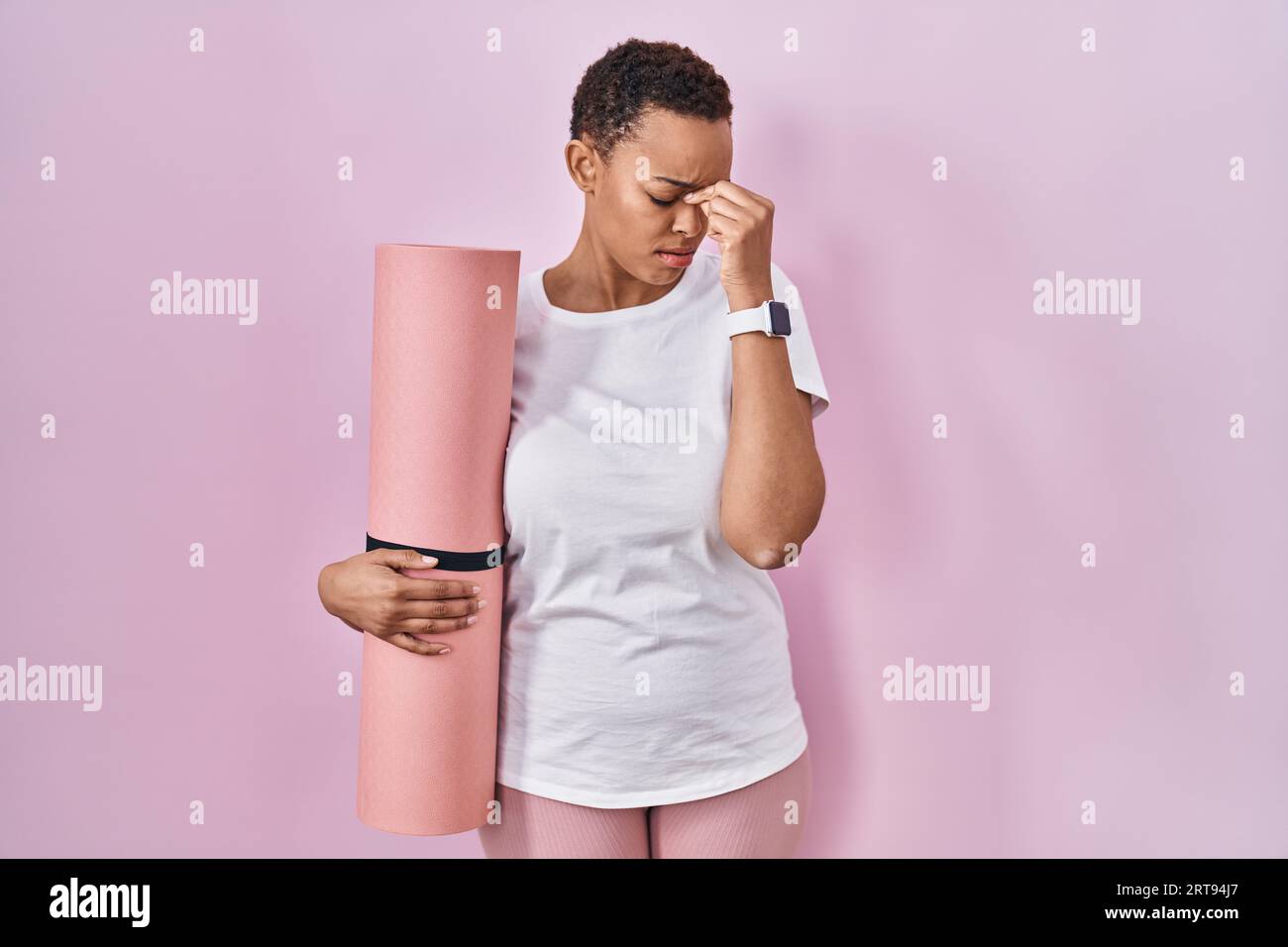 Bella donna afroamericana che tiene un tappetino yoga stanca che strofina il naso e gli occhi sentono affaticamento e mal di testa. concetto di stress e frustrazione. Foto Stock