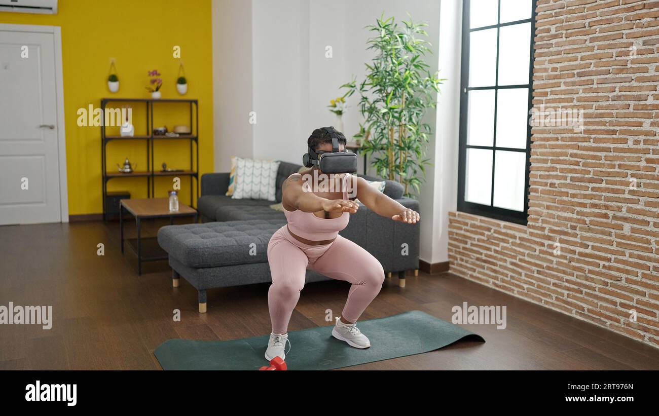 Donne afro-americane allenano le gambe utilizzando occhiali per realtà virtuale a casa Foto Stock