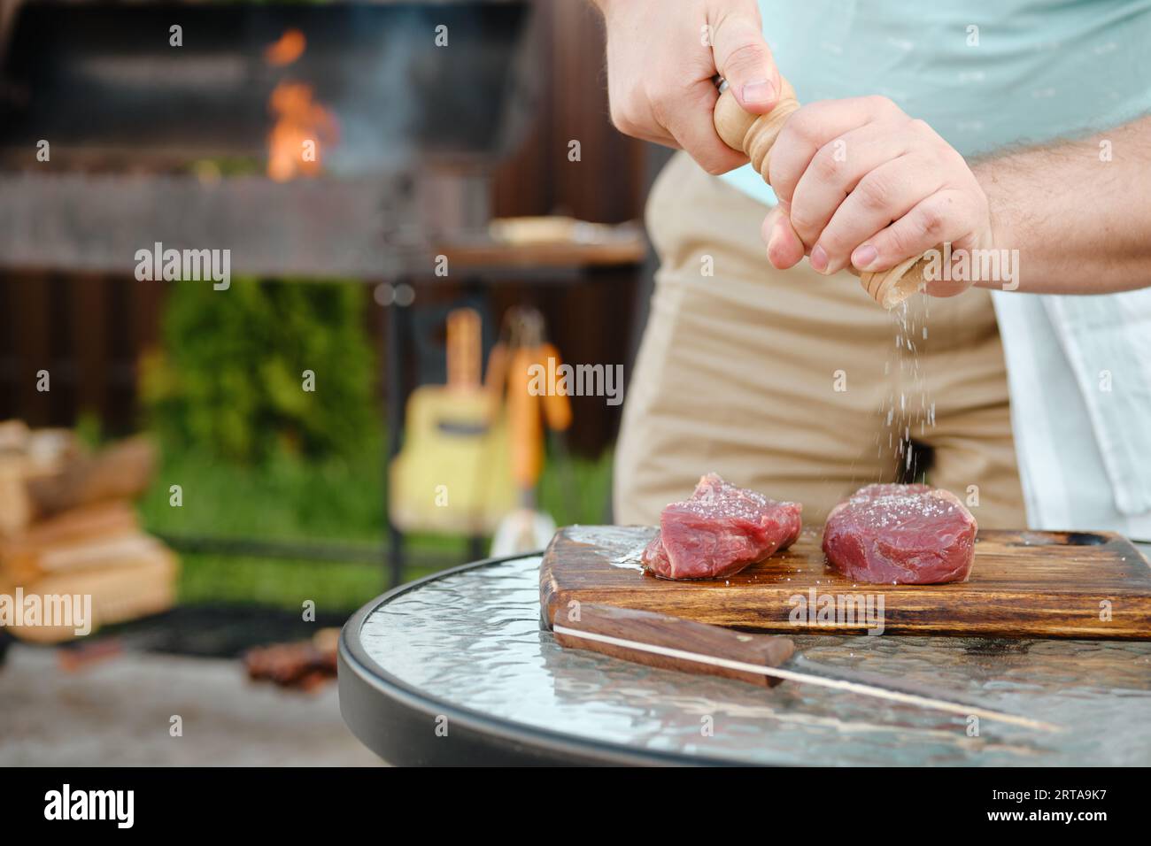 Uomo non riconoscibile che usa il mulino a mano per condire bistecca cruda con sale (foto con profondità di campo bassa) Foto Stock