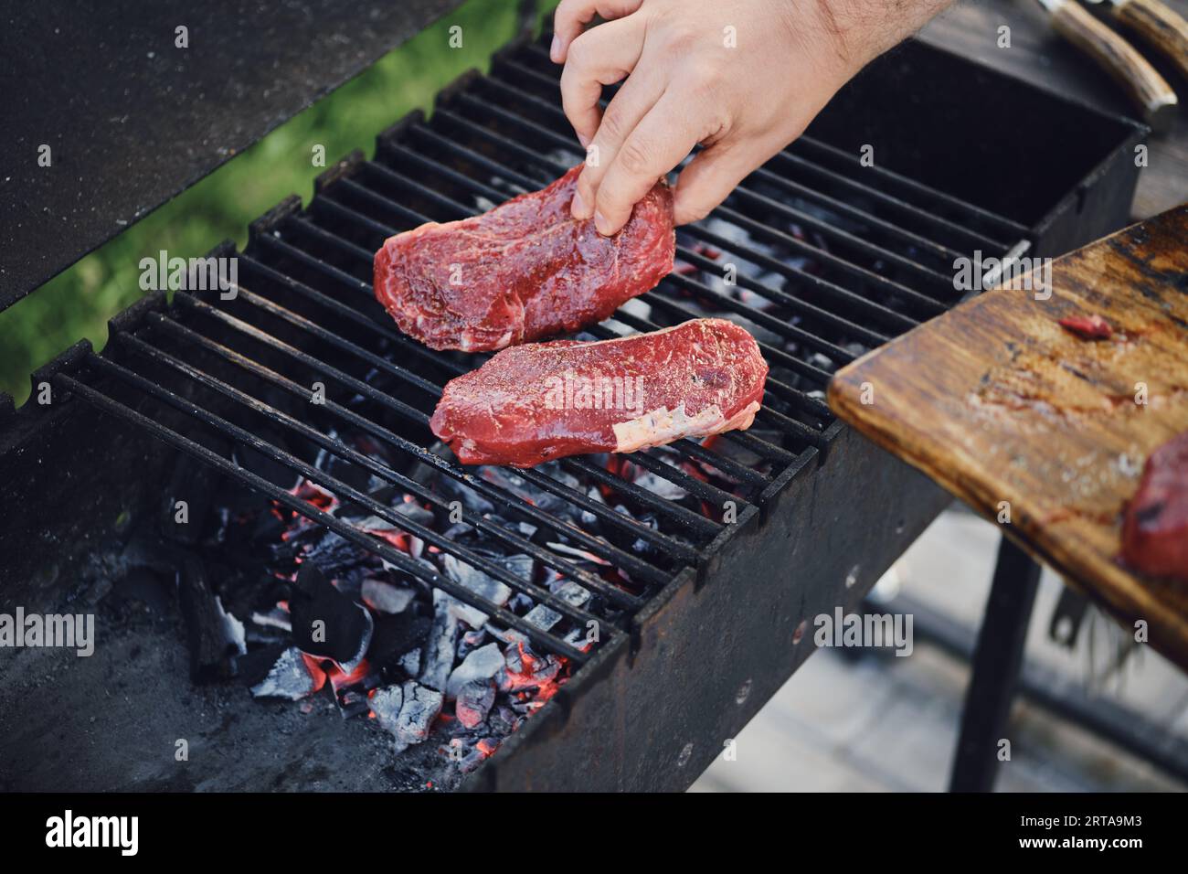 Un uomo irriconoscibile ha messo delle bistecche crude sulla griglia calda del grill Foto Stock