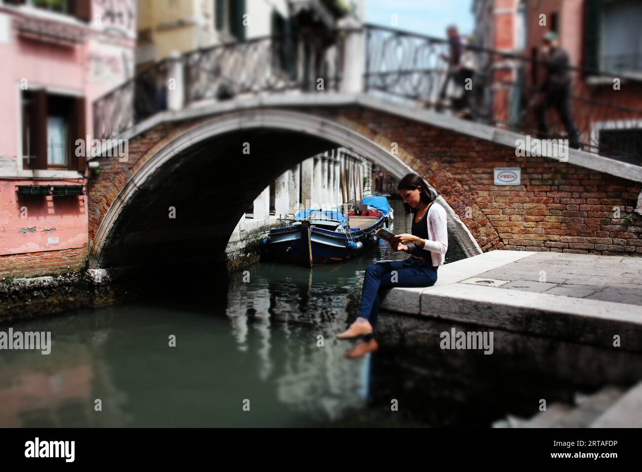 Una giovane ragazza seduta a leggere in un canale a Venezia, in Italia Foto Stock