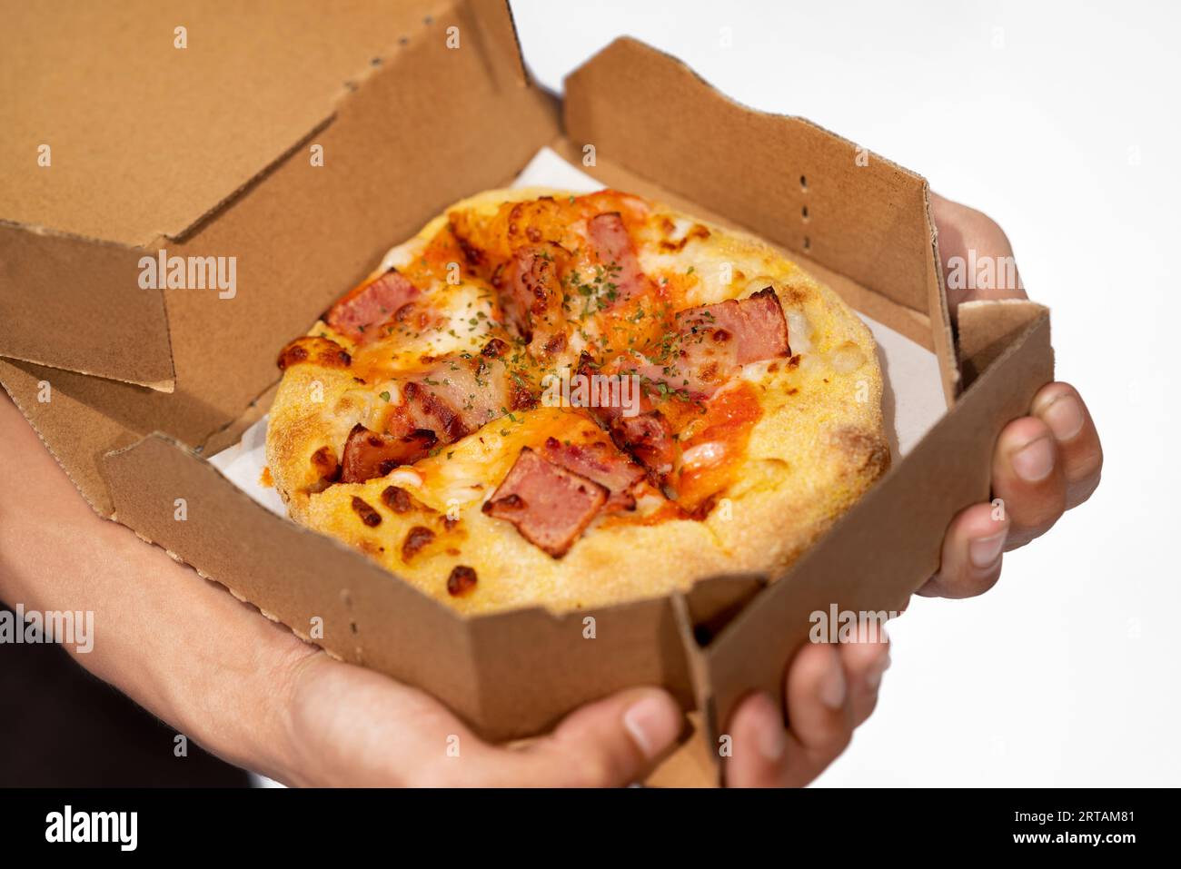 Una mano umana che tiene la pizza su una scatola di cartone con uno sfondo bianco Foto Stock