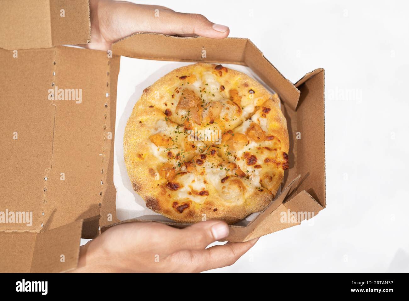 Una mano umana che tiene la pizza su una scatola di cartone con uno sfondo bianco Foto Stock