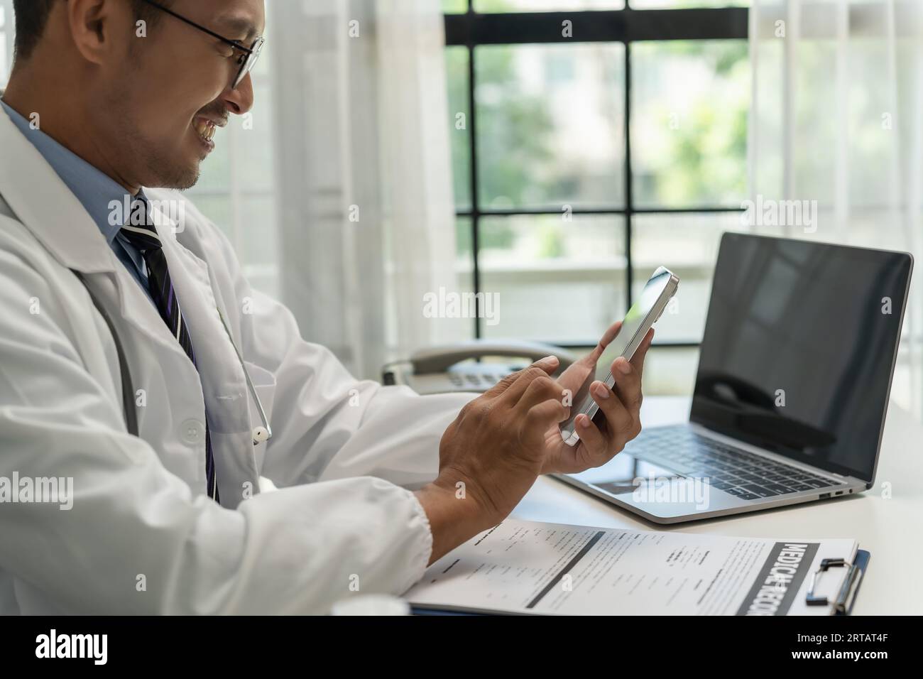 Medico sorridente che lavora con telefoni cellulari e servizi online remoti presso la clinica medico intelligente concetto di servizio di alta qualità Foto Stock