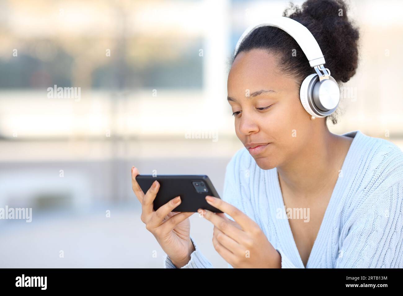 Donna di colore che indossa le cuffie per guardare video su un telefono orizzontale in strada Foto Stock