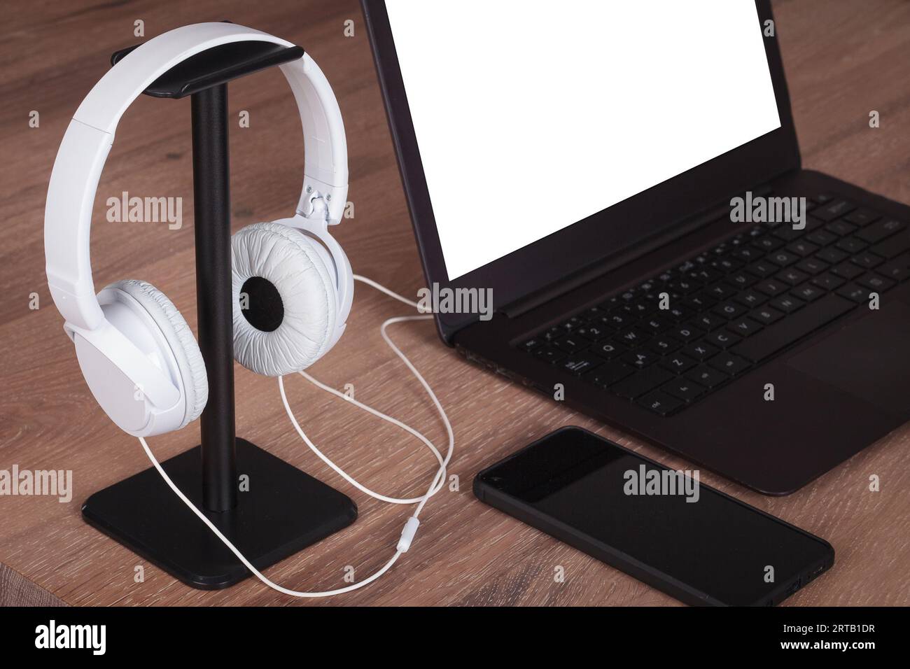 Moderna scrivania da ufficio con notebook e cuffie bianche, schermo vuoto. Foto Stock