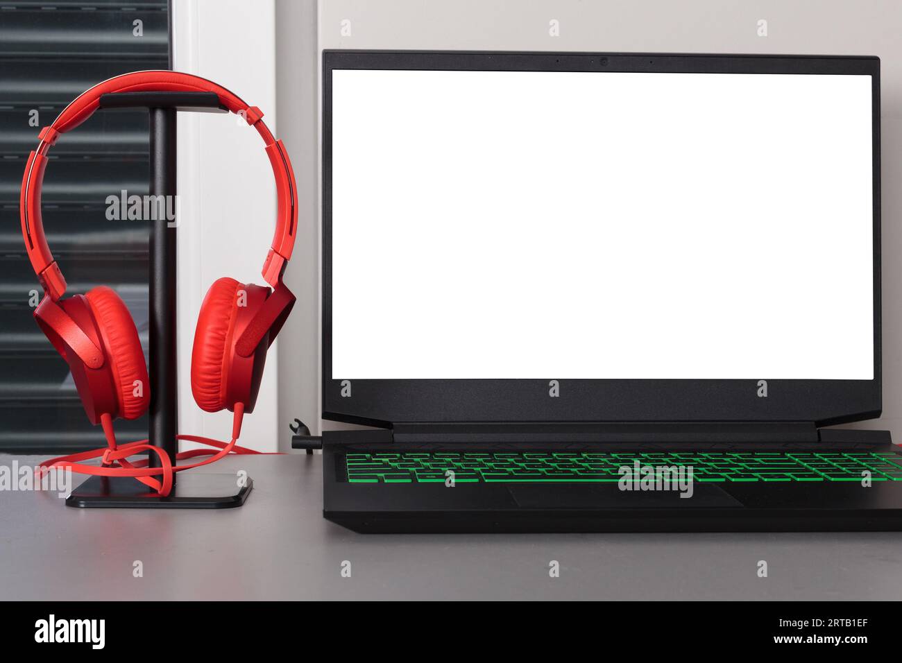 Configurazione da tavolo grigia con notebook e cuffie rosse. Schermo bianco vuoto. Foto Stock