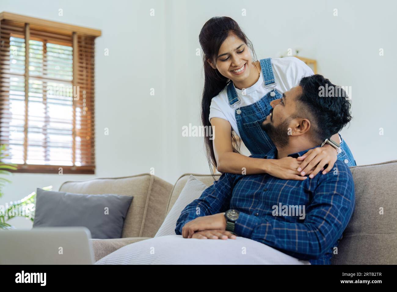 Una giovane moglie felice abbraccia il marito da dietro sul divano Foto Stock