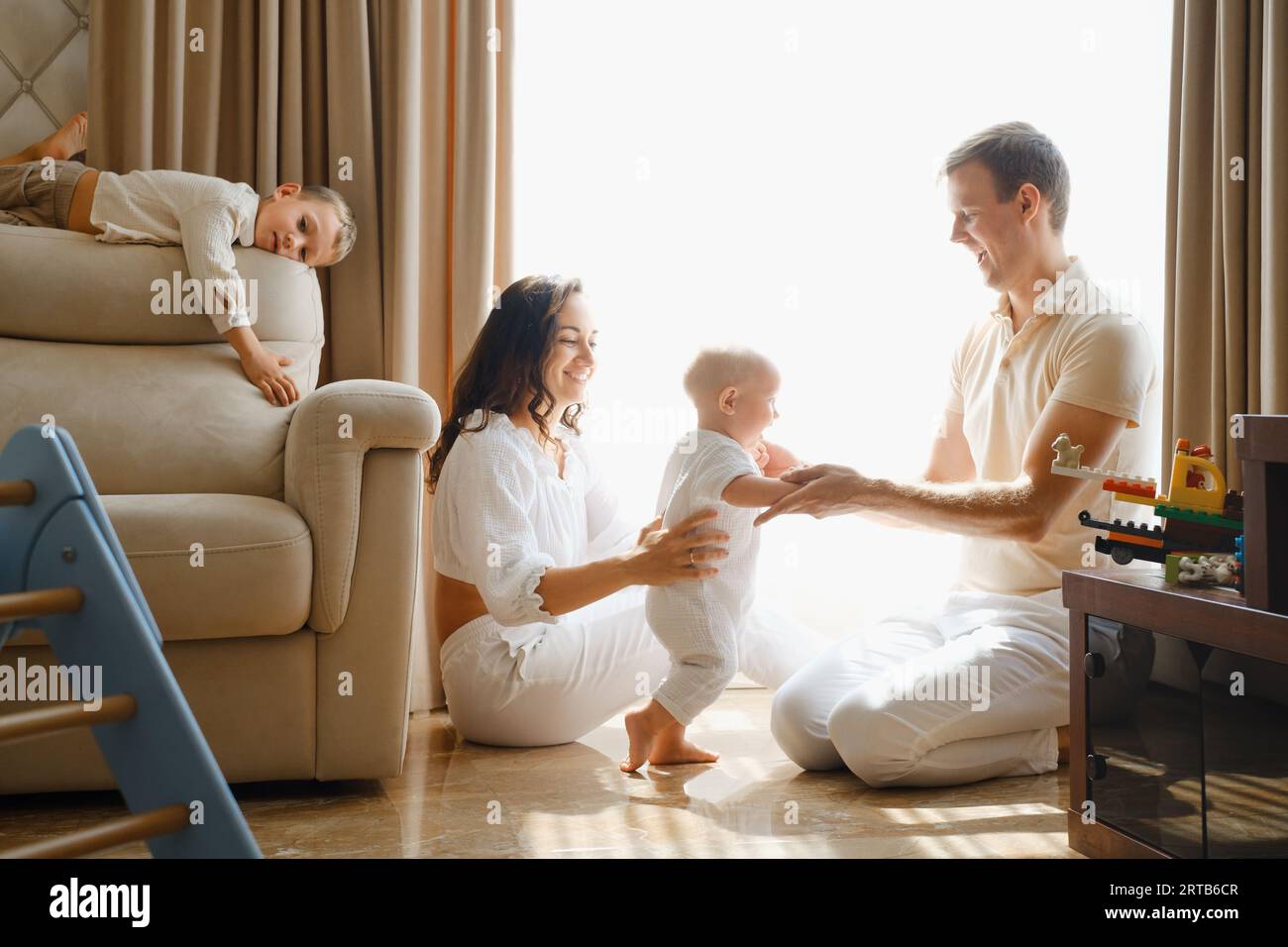 Famiglia con due bambini sul divano che si diverte. Mather, il padre, il bambino e i bambini piccoli sono felici la mattina a Livingroom. Bambini che giocano con il paren Foto Stock