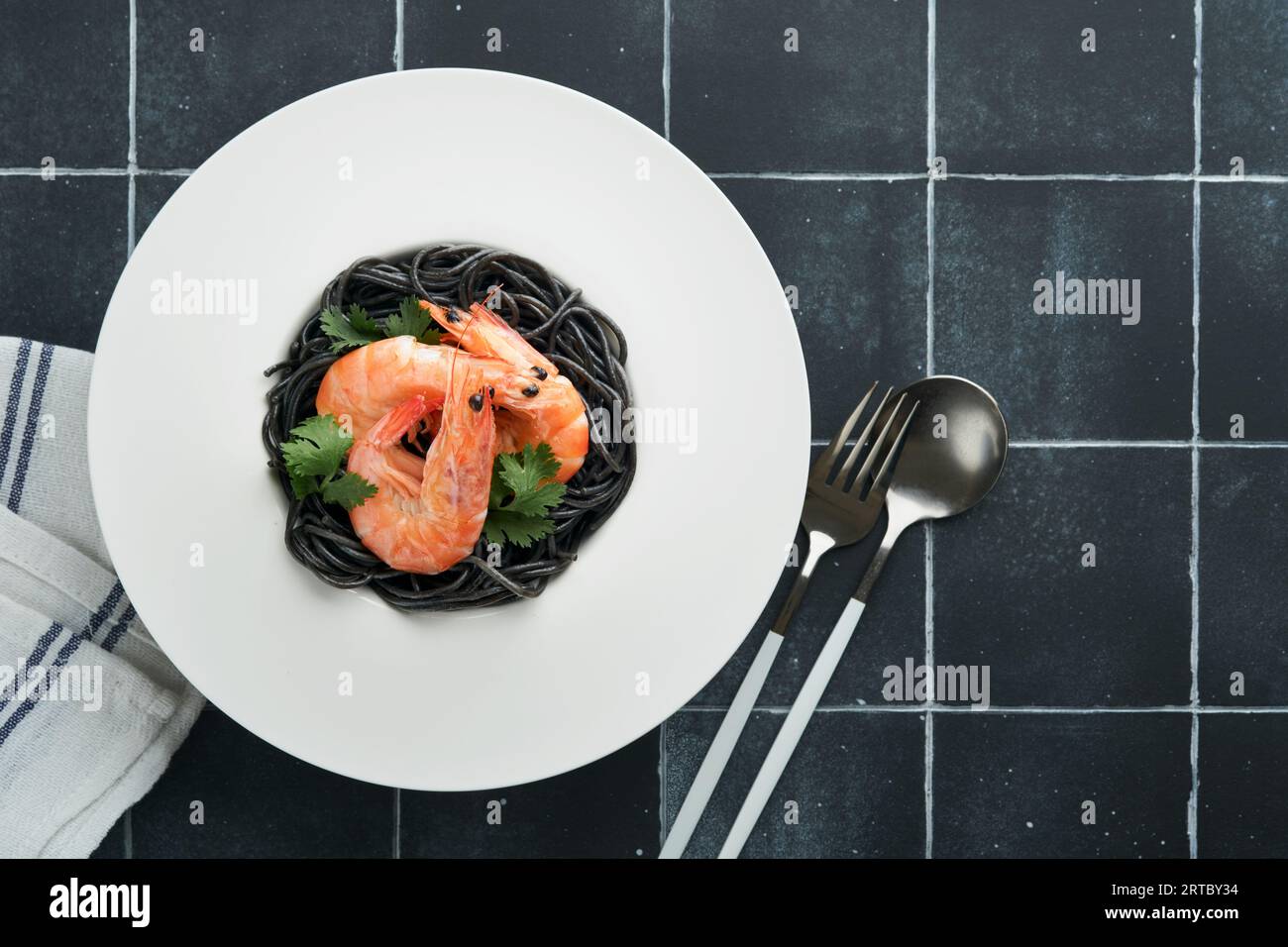 Spaghetti neri di gamberi su piatto nero su fondo scuro di cemento. Pasta con inchiostro calamaro e gamberi. Pasta a base di pesce. Vista dall'alto sulla linguetta in pietra nera Foto Stock