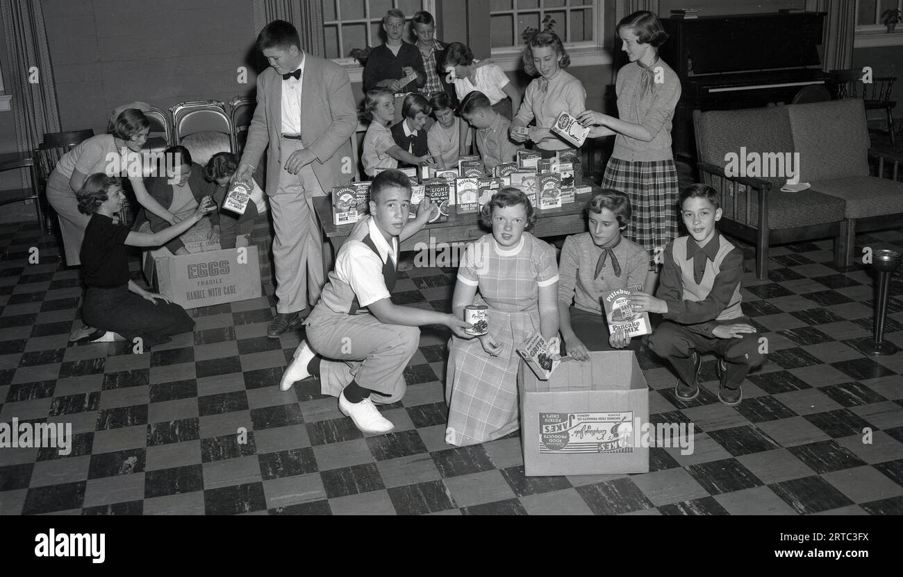 Anni '1950, giovani americani storici che guardano prodotti da forno casalinghi in un centro giovanile, USA. I prodotti includono: pillsbury, pancake mix, hot roll mix, fiocchi d'avena arricchiti di zia Jemima. Betty Crocker cake mix, una scatola vuota di patatine di jakes. Foto Stock