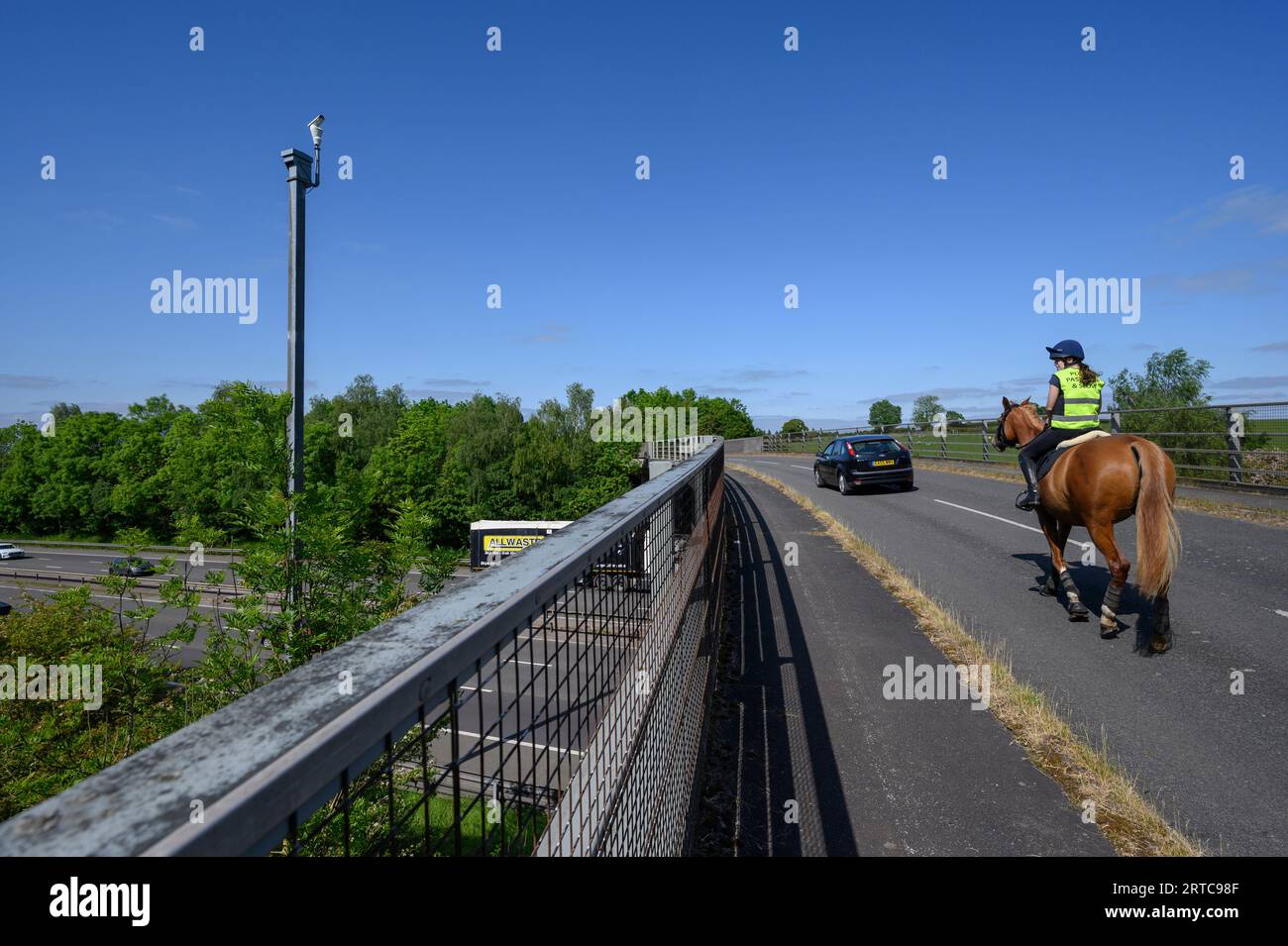 Auto che passa cavallo e cavaliere su un ponte stradale che attraversa l'autostrada M40, Warwickshire, Inghilterra. Foto Stock