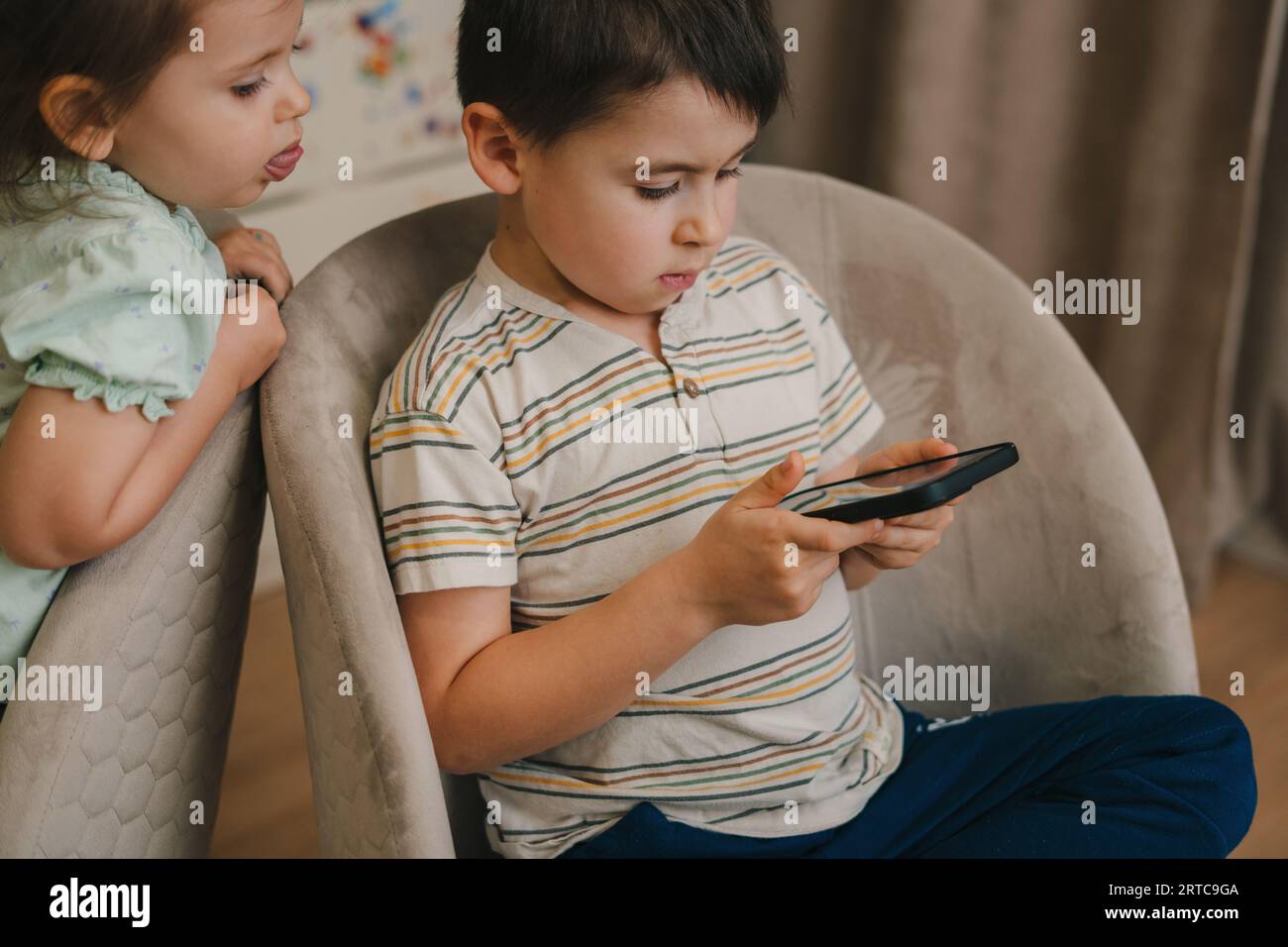 Due telefoni per bambini che usano il telefono insieme seduti sulle poltrone. Concetto di dipendenza da smartphone. Bella famiglia. Giocare a bambino. Gioca online Foto Stock