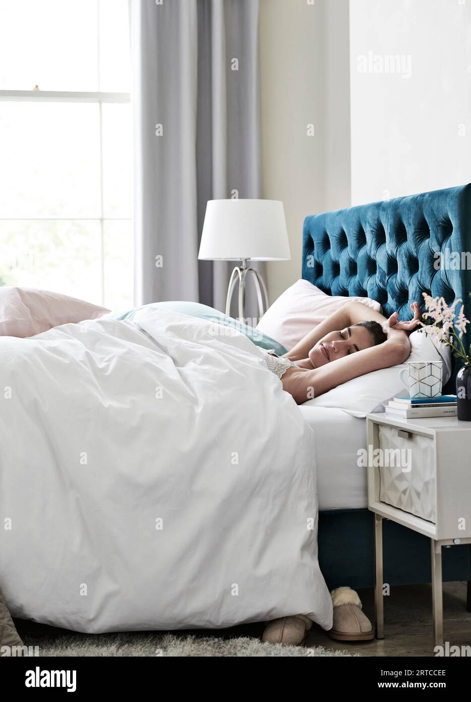 Bellissimo modello giovane che si prepara per il letto, dorme in camera da letto con biancheria da letto e tende con finestra, piumone, cuscini stile di vita, sereno e rilassato Foto Stock