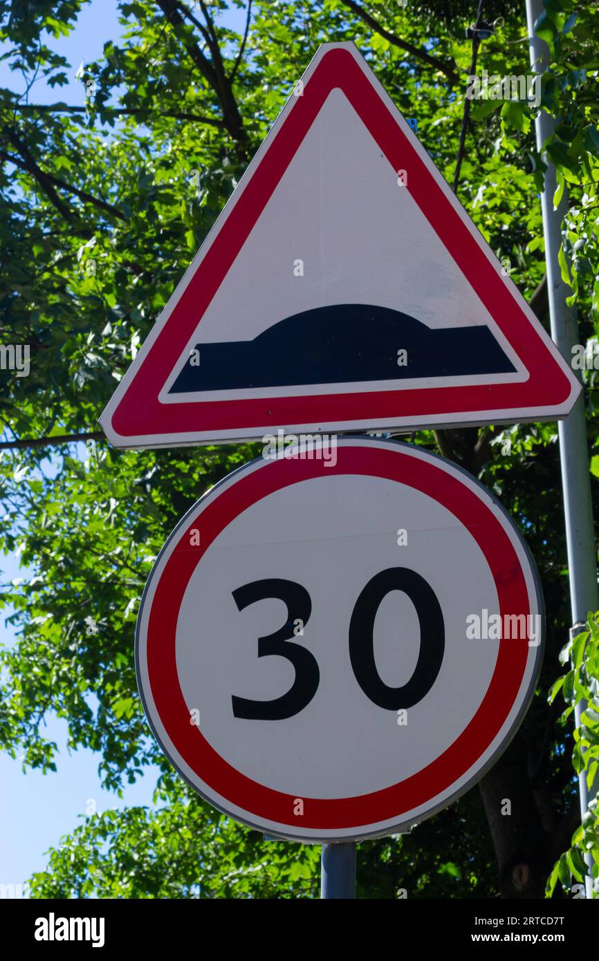 segnaletica stradale sconnessa e limite di velocità su sfondo di alberi verdi e cielo blu. Foto Stock