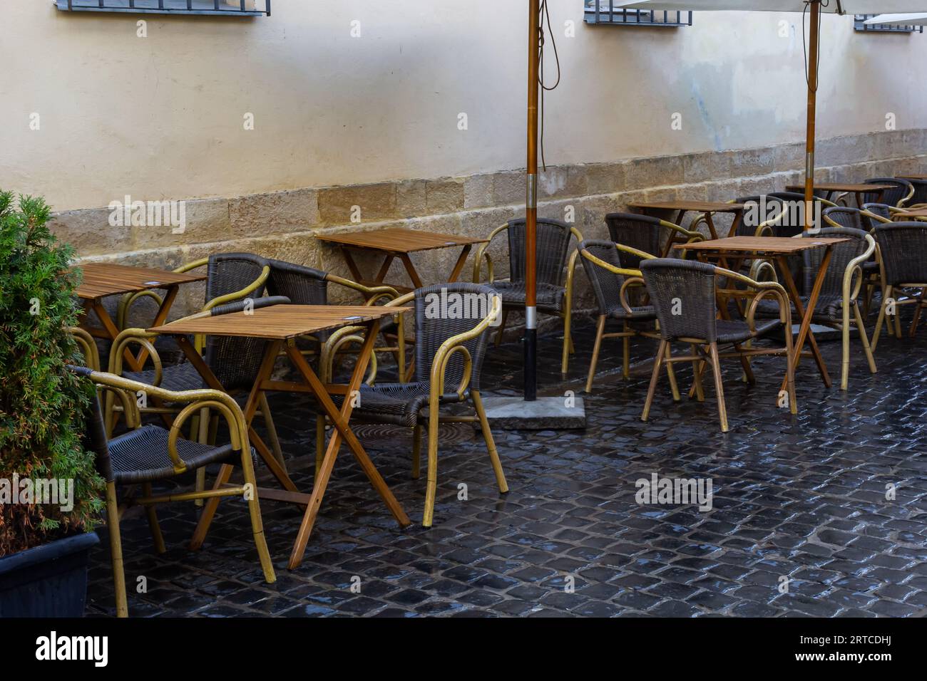 Tavolo e sedie in legno bagnato vuoti sulla terrazza della caffetteria all'aperto durante la pioggia. Vita cittadina di strada sotto la pioggia. Foto Stock